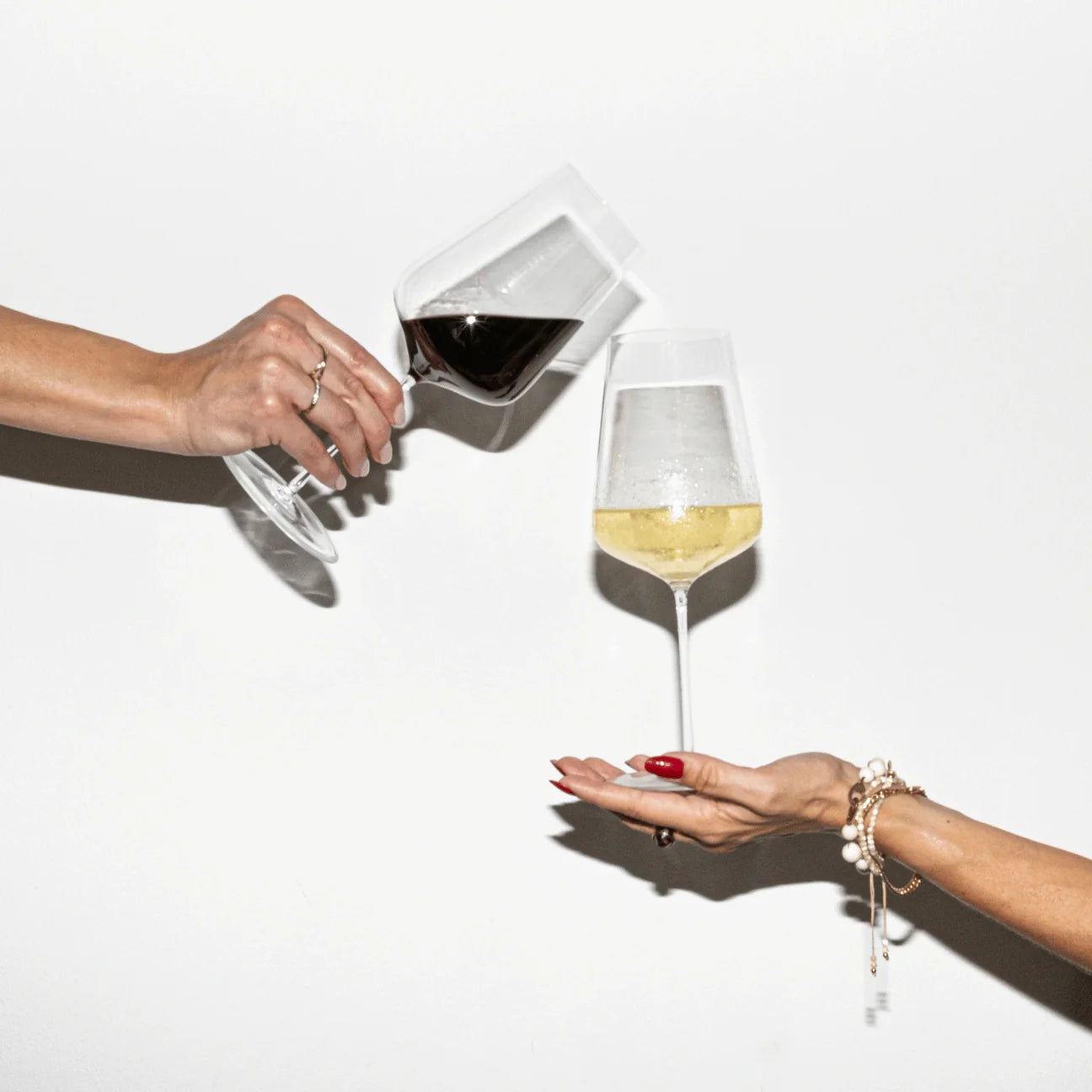 Hands of the two CUVÉE CANDLES founders and sisters Katharina and Miriam toasting each other with a red Cabernet Sauvignon and white Sauvignon Blanc in a Zalto glass.