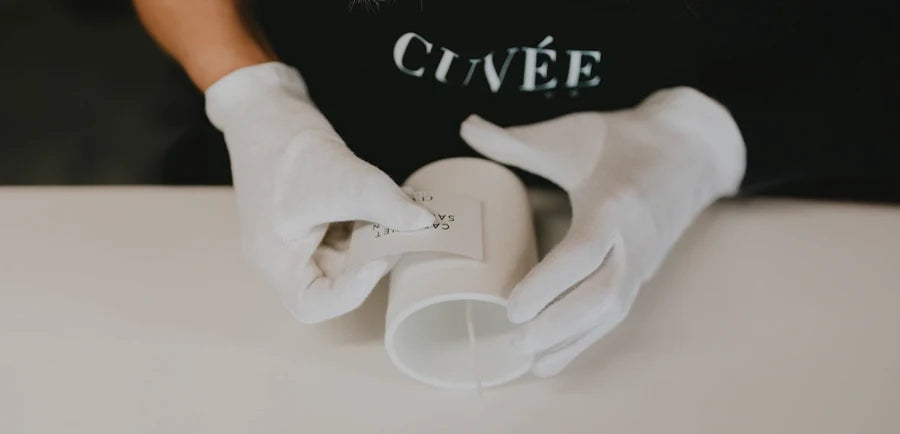 Careful handwork when attaching the elegant labels of the German luxury scented candles from CUVÉE CANDLES in white cotton gloves.